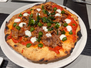Montanara napoletana fritta e poi cotta al forno condita con ragù di pomodoro napoletano, carne cotta nel ragù, basilico e mozzarella appena servita in una pizzeria