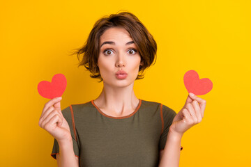Photo of nice girl with bob hairstyle dressed khaki t-shirt hold two paper hearts send kiss to you isolated on yellow color background