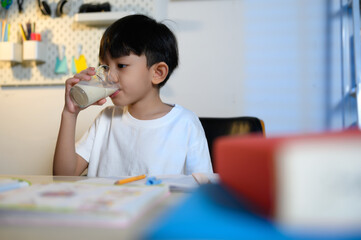 Asian Children's Student Drinking Milk Break After Learning for Refreshment at Home, Early Education, Studying, and Healthy Habits at Home.