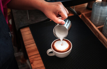 Fototapeta na wymiar Barista hand pouring milk into coffee making a cappuccino. Professional barista preparing coffee on the counter.