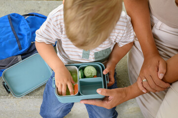 blond-haired boy holding container of food. back to school. homemade meals.