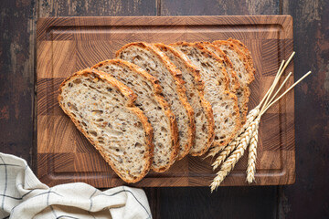 Whole wheat artisan sourdough bread sliced on a wooden cutting board, top view. Healthy bread - obrazy, fototapety, plakaty