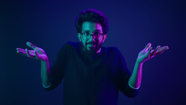 Male portrait in blue neon ultraviolet background Indian man shrug shoulders don't know gesture Arabian male guy confused unsure doubtful shrugging doubt uncertain guess puzzled bemused no clue sign