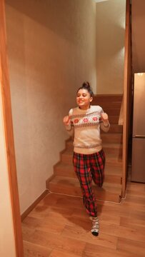 Young adult girl running to shake presents under the Christmas tree at morning. Young girl having fun with gifts near the Christmas tree at home.