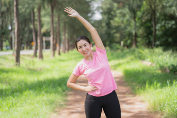 Asian woman wearing pink gym clothes Camlang warm up and stretch before running at the park.
