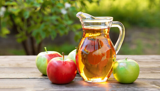 apple vinegar in glass pitcher and ripe fresh apples on wooden table outdoors