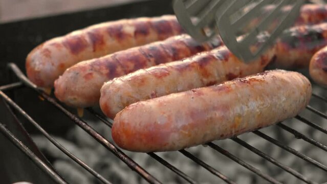 Grilled sausages. Cook man preparing grilling food bbq. Barbecue with smoke, flame outdoors. Tasty juicy german bratwurst. Charcoal kettle grill outside in backyard. Family summer vacation. Close-up