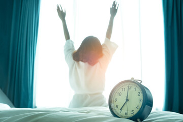 Morning of a new day, alarm clock wake up woman sitting in the room. A woman stretch the muscles at...