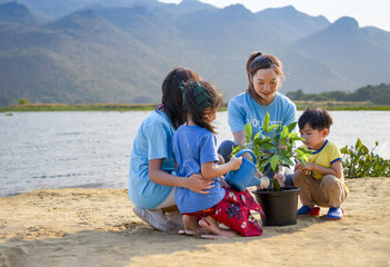 female volunteer joins planting tree with kids and teen by the river in community to instill...