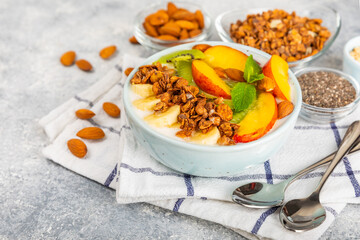 Granola bowl with yogurt and fresh almonds, blueberries, raspberries,peach, kiwi, strawberries and banana on textured kitchen table.Acai and spirulina bowl.Healthy breakfast concept. Copy space.