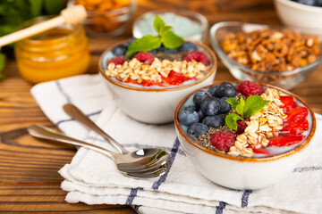 Granola bowl with yogurt and fresh almonds, blueberries, raspberries,peach and strawberries on a brown kitchen table.Acai and spirulina bowl.Healthy breakfast concept.