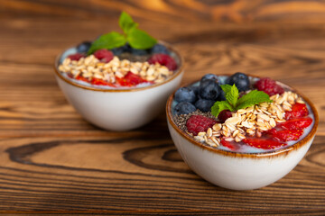Granola bowl with yogurt and fresh almonds, blueberries, raspberries,peach and strawberries on a brown kitchen table.Acai and spirulina bowl.Healthy breakfast concept.