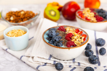 Granola bowl with yogurt and fresh almonds, blueberries, raspberries,peach and strawberries on a marble kitchen table.Acai and spirulina bowl.Healthy breakfast concept.copy space.Place for text.