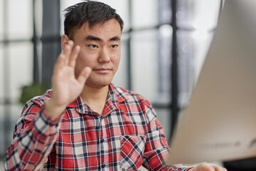 Cheerful multiracial man in casual wear using trendy laptop for video call, waving his hand greeting his diverse team