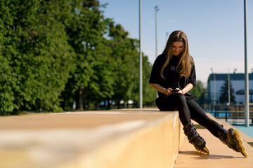 sports girl after rollerblading rests on the sports ground texting on the phone street sports...