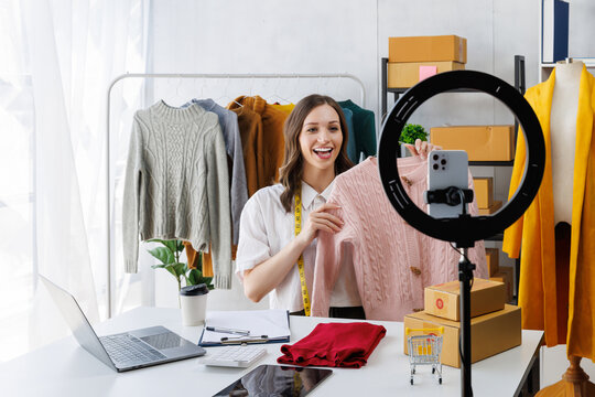 Beautiful woman describe selling clothes on camera live broadcast on social network at home, Online selling clothes on social media. Vlogger woman influencer, SME retail store owner.