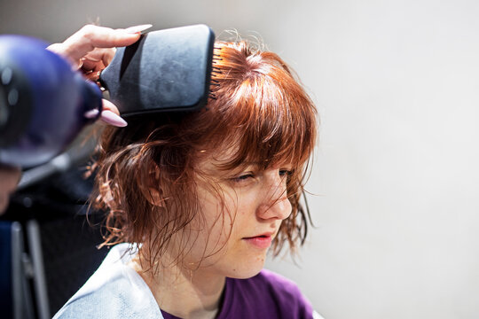 hairdresser combs the wet red hair of a teneyger girl after a haircut in a beauty salon on a light background