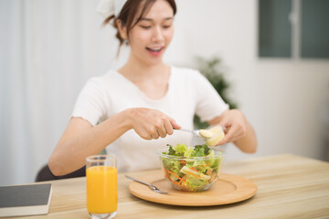 Happy beautiful Asian woman eating healthy food with vegan.salad in the kitchen at home.