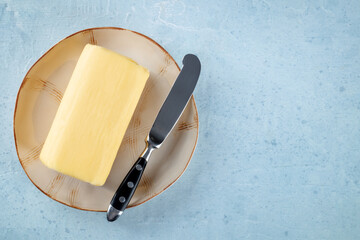 A block of butter with a knife on a plate, overhead flat lay shot on a light slate background, with...
