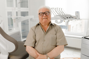 Charismatic old man patient have a oral care treatment at modern dental clinic he posing in front of the camera at dentist office he crossing hands and looking straight