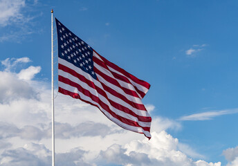 Large size USA flag stars and stripes blowing in wind with interesting clouds behind in blue sky