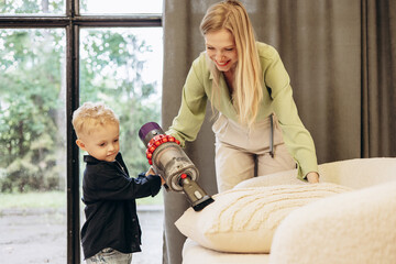 Mother with her son vacuuming sofa at home