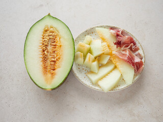 Melon cut in half beside plate with chunks and slice of melon with ham. Typical Spanish tapa as a...