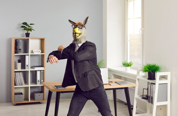 Lazy corporate employee has fun at end of work day, wants to party and behaves like animal. Happy funny excited guy dancing in office wearing unusual bizarre silly wacky rubber donkey mask and glasses