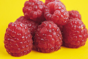 Heap of fresh ripe and sweet raspberries on yellow background. Red raspberries. Macro shot.