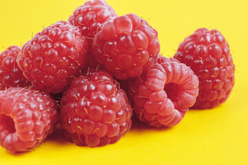 Heap of fresh ripe and sweet raspberries on yellow background. Red raspberries. Macro shot.