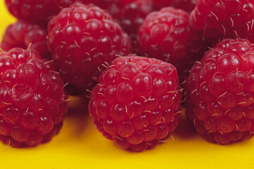Heap of fresh ripe and sweet raspberries on yellow background. Red raspberries. Macro shot.