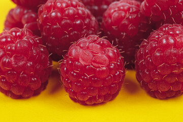Heap of fresh ripe and sweet raspberries on yellow background. Red raspberries. Macro shot.