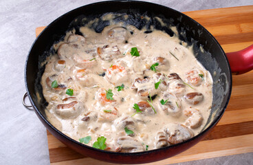 Cooking shrimps in creamy sauce with champignons in a pan. Seafood meal preparation