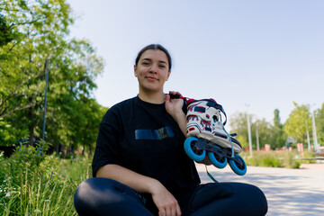 portrait of young smiling hipster girl in skate park holding roller skates in hands before starting...