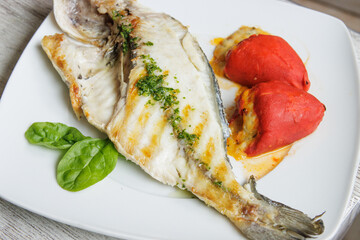 Grilled gilt-head bream on a white plate accompanied by stuffed piquillo peppers