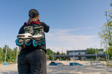 young hipster girl carries roller skates before starting training lesson on sports field street...