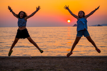 Silhouette of children jumping at sunset on a beach.