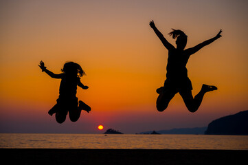 Silhouette of mother and children jumping at sunset on a beach.