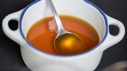 Smooth golden honey with a spoon inside the white bowl
