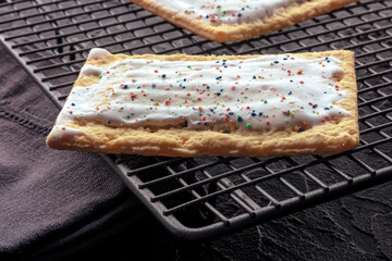 Pop tart on a baking rack. A poptart toaster pastry with icing on a black background - obrazy, fototapety, plakaty