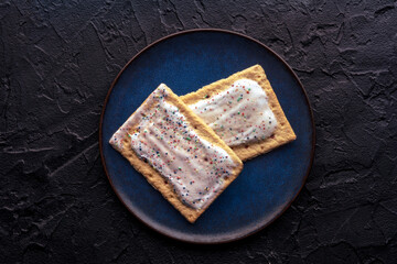 Pop tarts on a plate. Poptart toaster pastry with icing on a black slate background, overhead flat lay shot