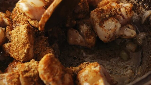 Cholent in a cast iron pan is stirred with a wooden spatula. Close-up