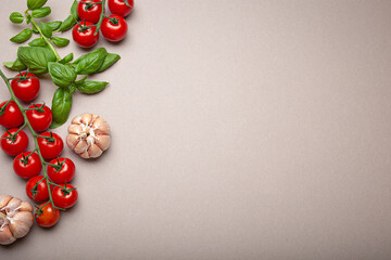 Composition with branch of fresh cherry tomatoes, basil, garlic cloves, lemon wedges, on minimalistic gray clean background, overhead shot with copy space