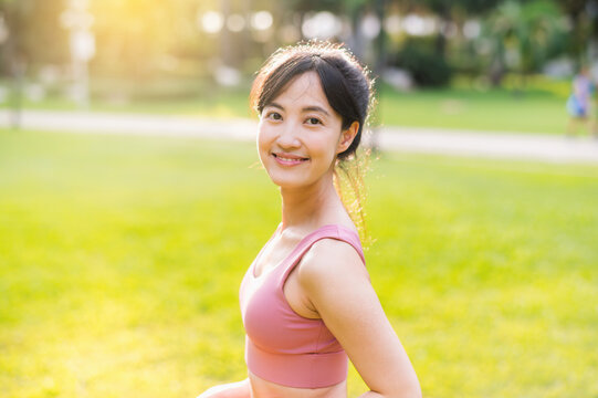 Capture the essence of wellness living with a happy, young 30s Asian woman smiling at the camera in a park at sunset. Embrace the beauty of wellness.