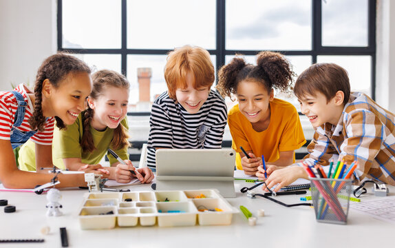 Cheerful  schoolkids   looking at tablet screen and celebrate   successful completion of collective school work   during online lesson