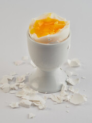 Broken and peeled white egg with runny yolk in a white egg cup