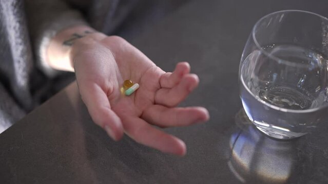 Close-up shaking female palm with pills on tabletop with glass of water. Closeup high angle view unrecognizable woman with antidepressant drugs leaving in slow motion