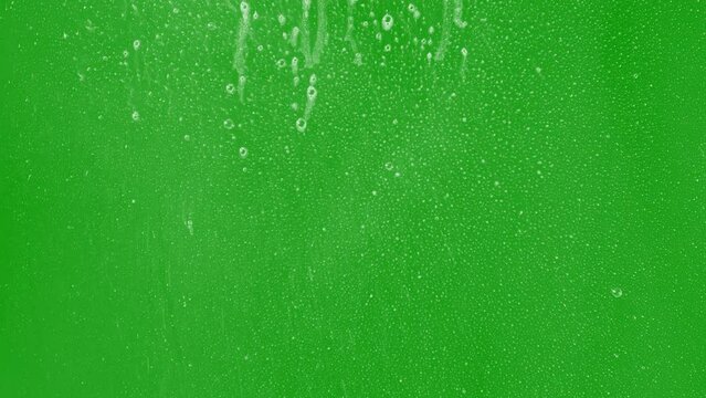 Foam dripping on glass with a greenscreen background with small bubbles and mist