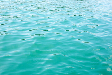 Abstract nature textured background, water waves in the lake with sun reflection, clear blue-green water