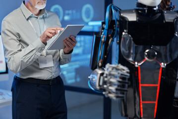 Close-up of mature engineer using digital tablet to connect with robot during his work in the lab